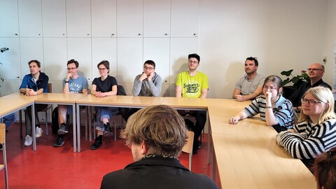 Die Teilnehmenden der Summer School sitzen an einem U-förmigen Tisch und hören aufmerksam zu.