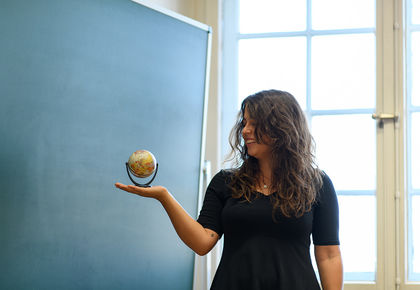Eine Studentin hält einen kleinen Globus vor einer Tafel auf ihrer Hand.
