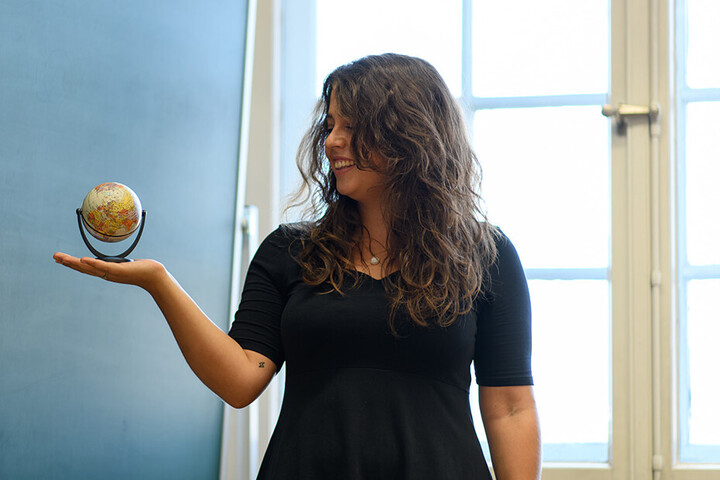Eine Studentin hält einen kleinen Globus vor einer Tafel auf ihrer Hand.