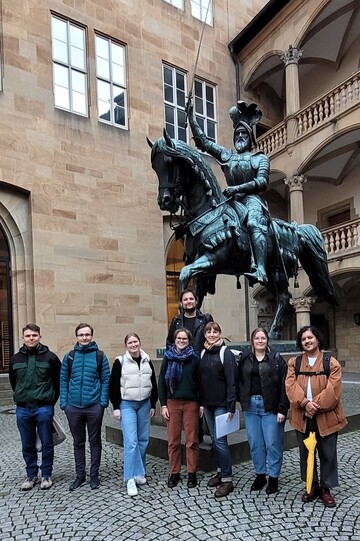 Eine Gruppe von acht Personen steht vor einer bronzenen Reiterstatue im gepflasterten Innenhof eines Renaissance-Schlosses.