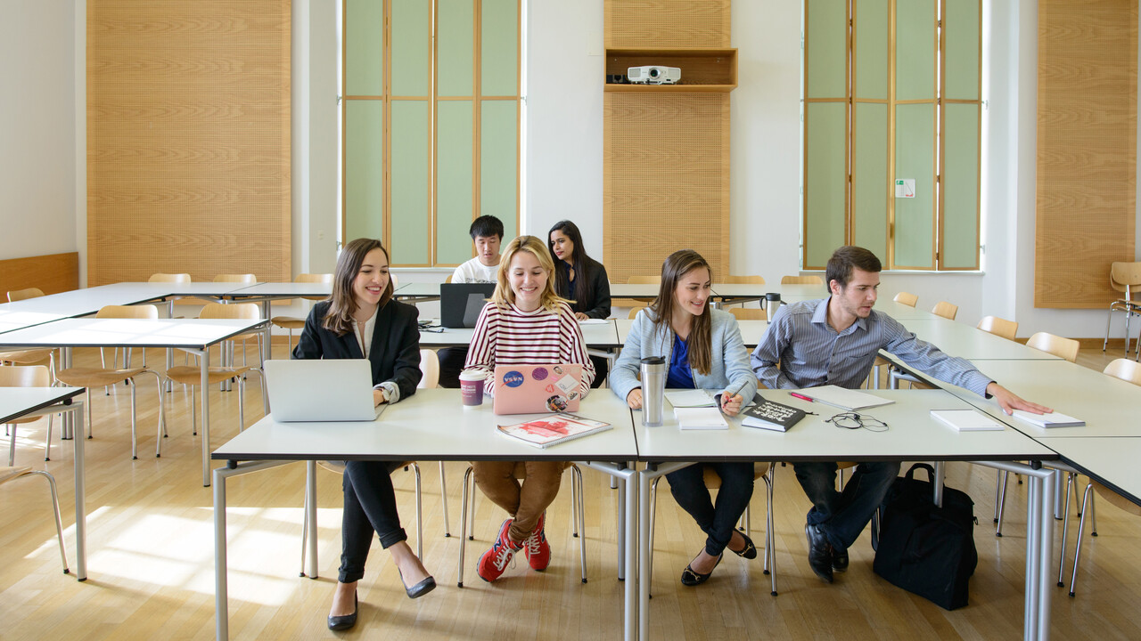 Sechs Studierende arbeiten in einem Seminarraum. Vor ihnen liegen Laptops, Notizblöcke und Bücher.