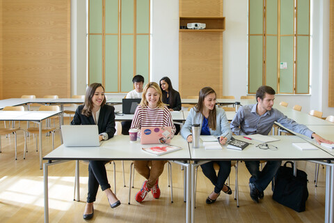 Sechs Studierende arbeiten in einem Seminarraum. Vor ihnen liegen Laptops, Notizblöcke und Bücher.