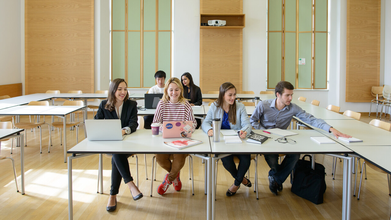 Sechs Studierende arbeiten in einem Seminarraum. Vor ihnen liegen Laptops, Notizblöcke und Bücher.