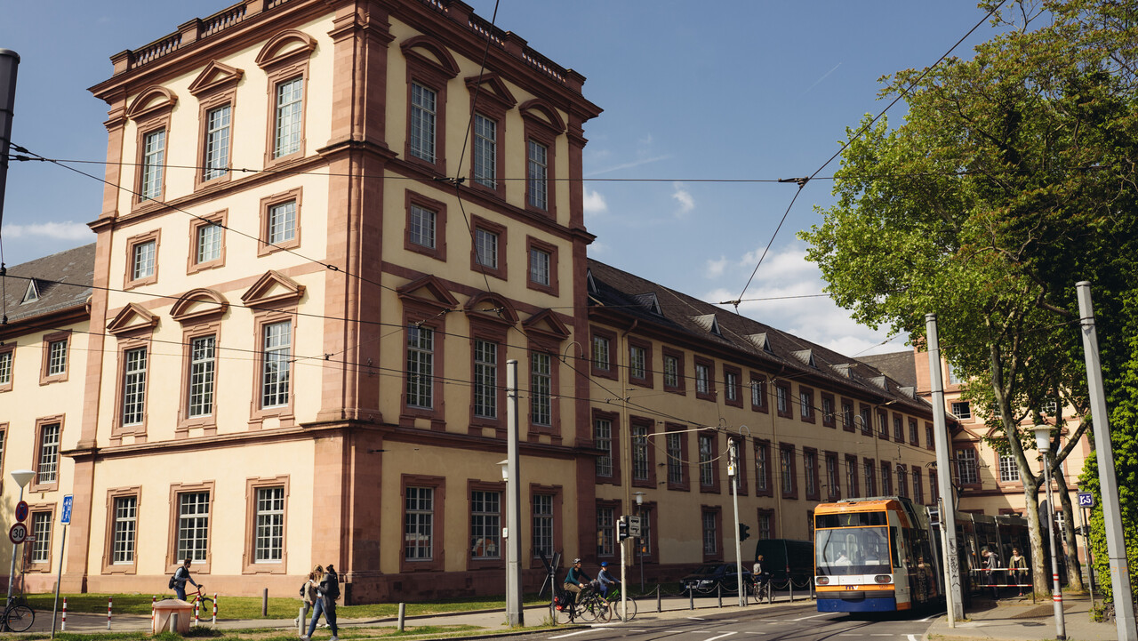 Der Eckturm am Ostflügel des fensterreichen Mannheimer Schlosses. Auf der Straße fahren eine Straßenbahn und Radfahrer.