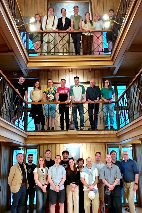 Ein Gruppenfoto der Teilnehmender der Summer School, die in einem holzgetäfelten Raum mit zwei Balkonen stehen.