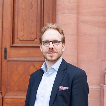 Dr. Martin Brecher. Er trägt ein dunkelblaues Sakko und steht im Ehrenhof des Mannheimer Schlosses.