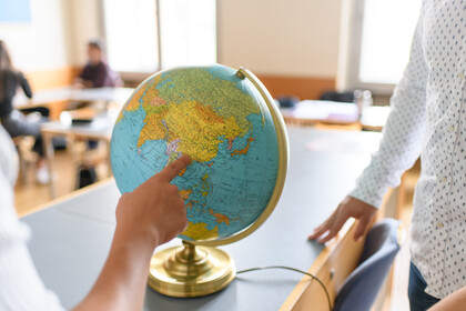 Eine Hand zeigt auf einen Globus, der auf einem Tisch steht