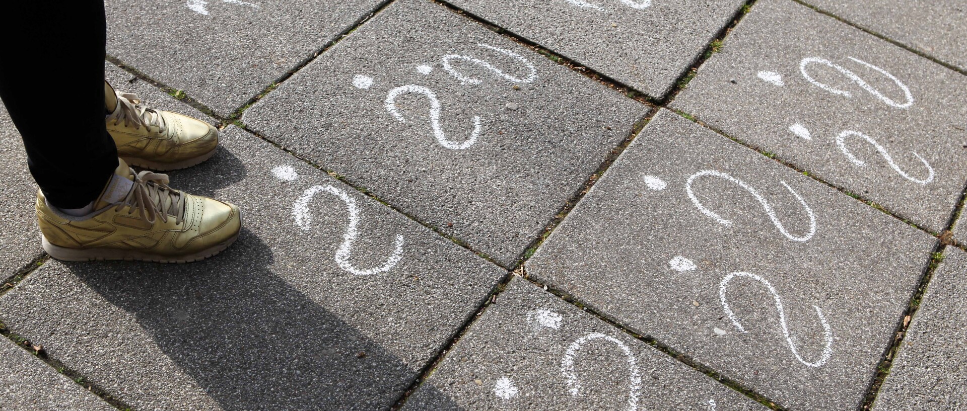 Eine Person steht vor lauter weißen Fragezeichen, die mit Kreide auf den Boden gemalt sind.