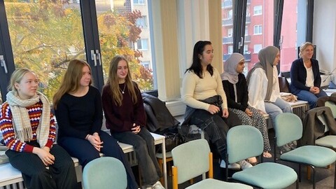 Schüler*innen sitzen in einem Seminarraum auf den Tischen vor dem Fenster. 