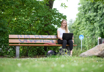 Studentin mit Laptop auf einer Parkbank