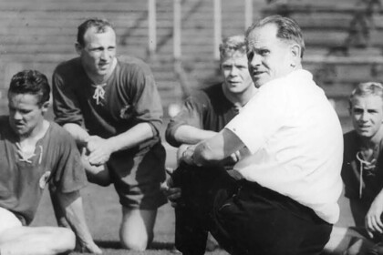 Flyer der Veranstaltung mit Informationen und Bild von Herberger im Trainingsgespräch mit 4 Fußballern, alle sitzen auf dem Rasen in einem Stadion