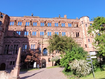 Ansicht des aus rotem Sandstein gebauten Ottheinrich-Baues mit zahlreichen Statuen an der Fassade vor blauem Himmel