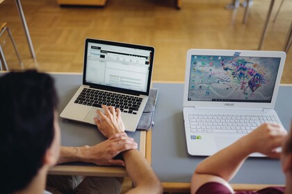 Zwei Studierende sitzen an einem Tisch und schauen auf ihre Laptop-Bildschirme