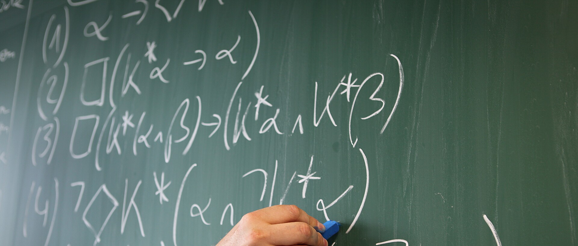 Hand with blue chalk on a green blackboard written with white formulas