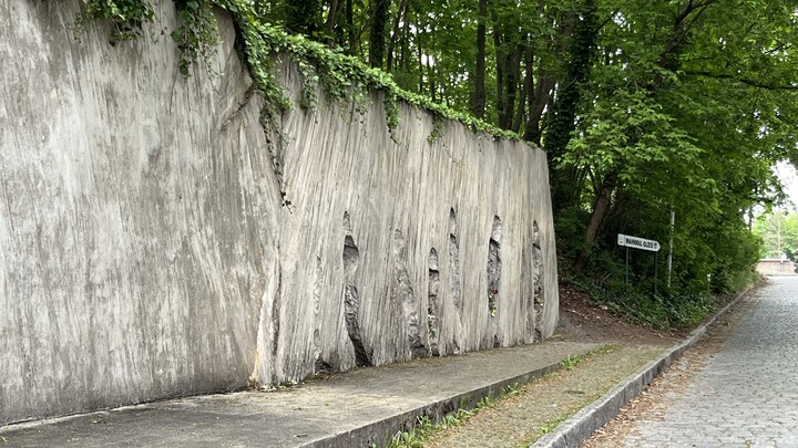 Künstlerische Installation am Mahnmals Gleis 17: Eine lange Betonwand, auf der Negative von Personen zu erkennen sind, die sich Richtung Bahnsteig bewegen.  