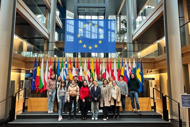 tudierendengruppe posiert im Europäischen Parlament vor einer Aufstellung europäischer Nationalflaggen und der Europaflagge